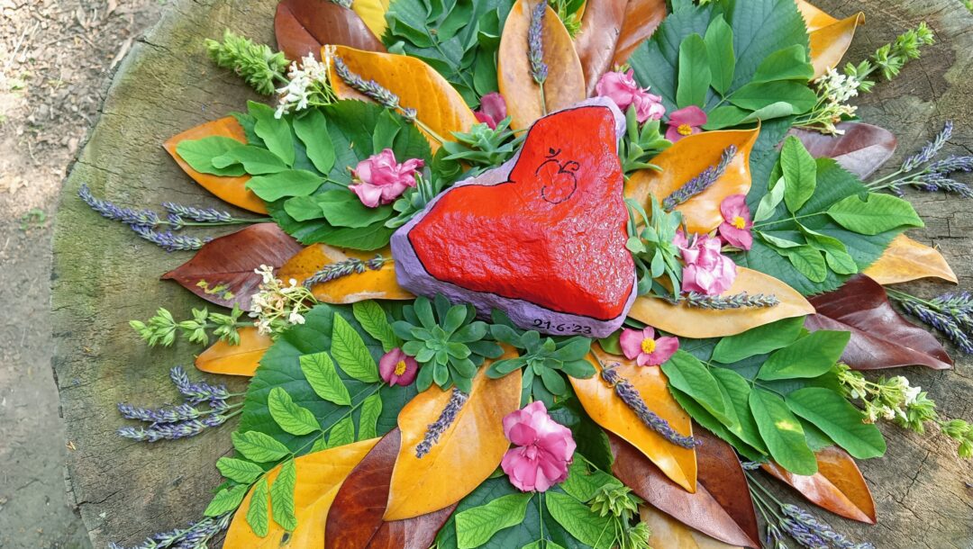 Cuore in pietra dipinto di rosso posto sopra una composizione di foglie e fiori